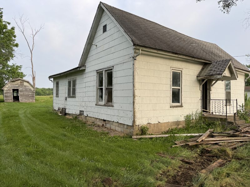 Framing lumber from a removed rear addition stacked beside a white farmhouse in Mid-Missouri during partial demolition