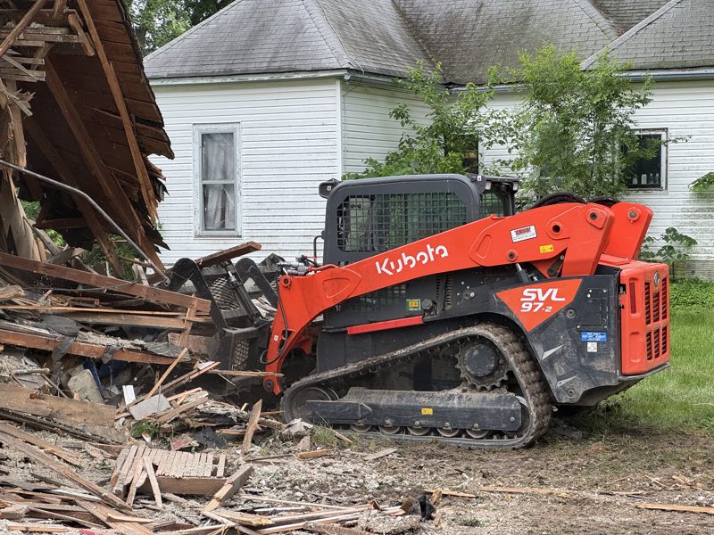 Kubota track loader working a demolition debris pile beside a house in Mid-Missouri during teardown and haul-off