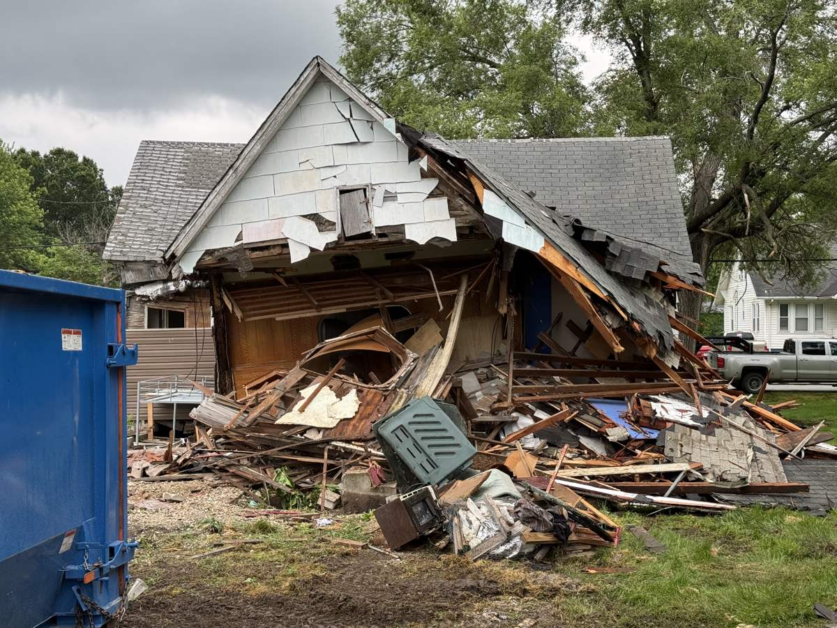 Atlas structural demolition in Mid-Missouri, a damaged single-story house mid-teardown with the roofline collapsed and debris staged beside the dumpster for haul-off