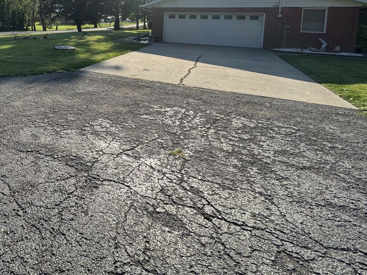 Alligator cracking spread across an asphalt surface next to a cracked concrete apron on a Mid-Missouri property, the kind of base failure that settles the parking lot replacement vs repair question in favor of replacement