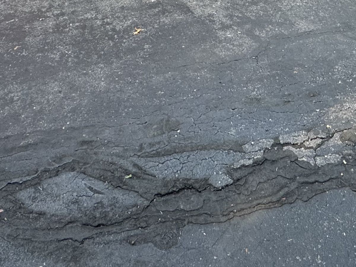 Asphalt surface patch breaking apart over a cracked base on a Columbia, MO property, a sign the repair never had support underneath it