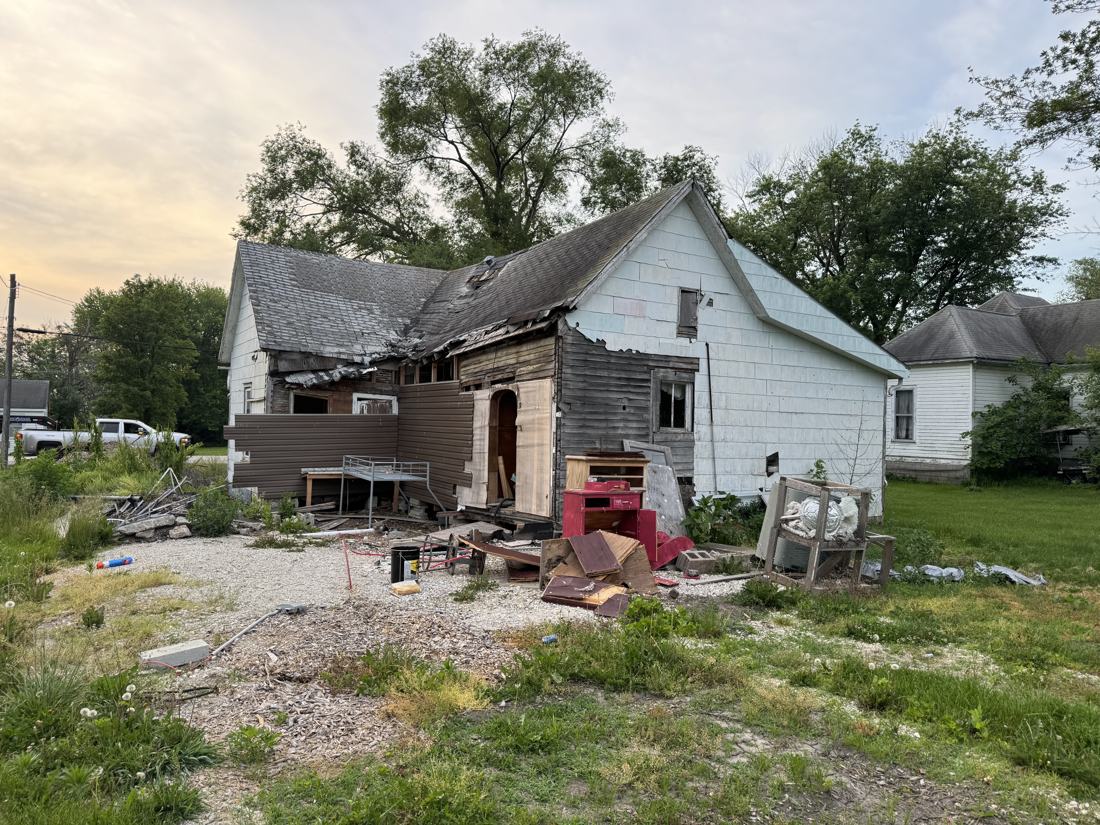 Partial demolition on a Mid-Missouri house with the rear addition torn off, the original exterior wall exposed, and debris staged on the gravel for haul-off