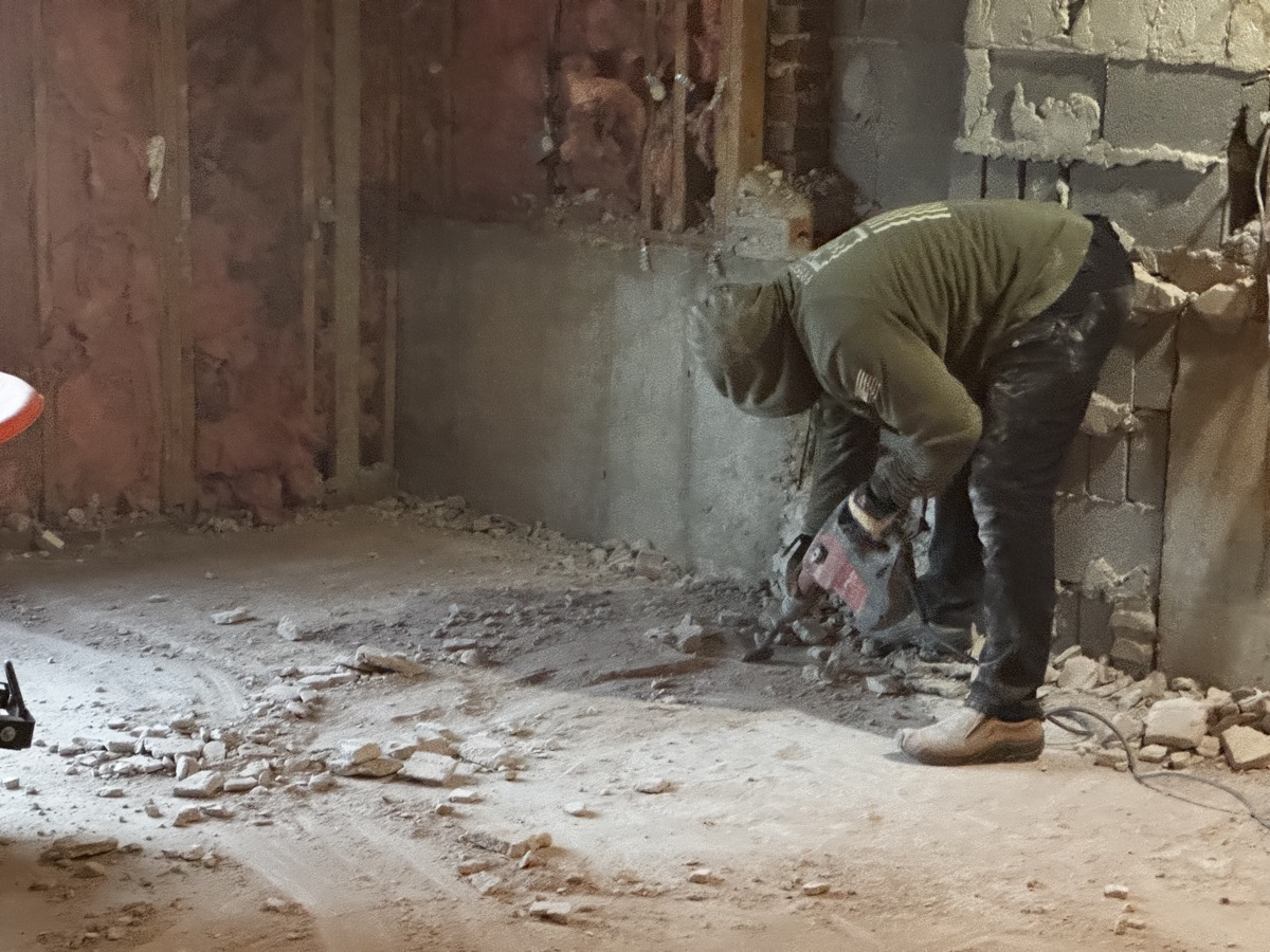 Worker breaking up concrete block wall during demolition project