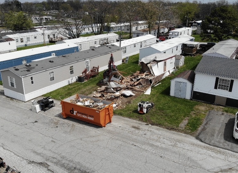 Excavator loading demolition debris into a haul truck at a residential demolition site in Columbia, MO