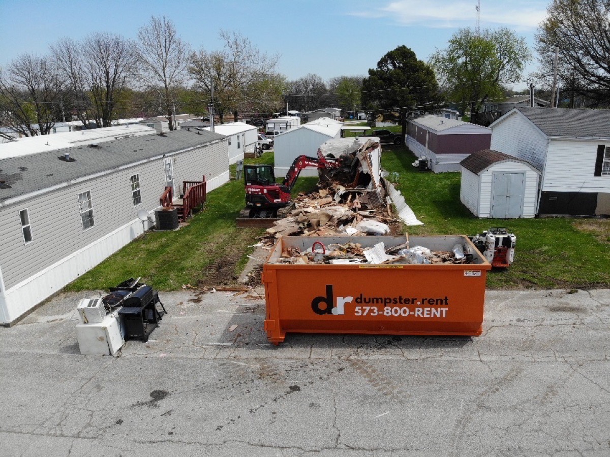 Aerial view of mobile home demolition in progress with excavator and dumpster